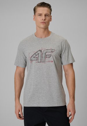 Mężczyzna w szarej koszulce z technicznym rysunkiem logo "4F", stojący na jednolitym szarym tle.