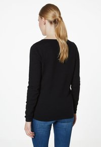 Pull en maille noire avec un col rond et des manches longues, présentant un motif texturé. Assorti à un jean en denim bleu.