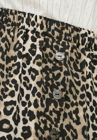 Sukně s leopardím potiskem a elastickým pasem, s černými a béžovými tóny, ozdobená třemi šedými knoflíky vpředu.