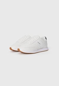 Weiße Sportschuhe aus glattem Leder mit einer Gummisohle und braunen Akzenten, flachen Schnürsenkeln und einem Logo an der Seite.