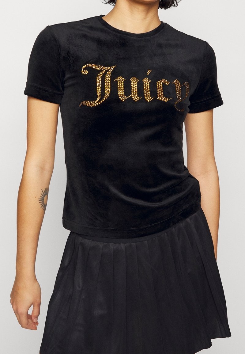 Svart sammet T-shirt med guldstrass "Juicy"-text. Korta ärmar och rundad halsringning. Matchad med en plisserad svart kjol.