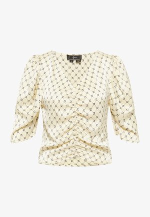 Sárga, mintás blúz rövid puffos ujjakkal, ráncolt elülső résszel és finom fényességgel. Az egész felületen fekete geometriai minta található.