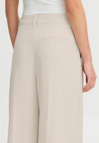 Beige wijde pantalon met een zachte textuur, voorzien van een slanke tailleband, subtiele achterzakken en strakke lijnen voor een minimalistisch ontwerp.