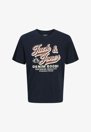 camiseta de algodón azul marino con texto gráfico blanco y rojo "Jack & Jones DENIM GOODS" y jeans de mezclilla azul claro relajados. Zapatillas blancas.