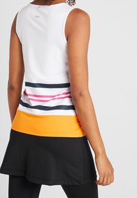 Top bianco senza maniche con righe orizzontali rosa, blu navy e arancione all'orlo, abbinato a uno skort nero. Tessuto liscio e elastico.