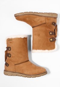 Ein Paar beige Wildleder-Winterstiefel in Midi-Länge mit weißem Fleecefutter, braunen Riemendetails und strukturierten Gummisohlen auf einem weißen Hintergrund.