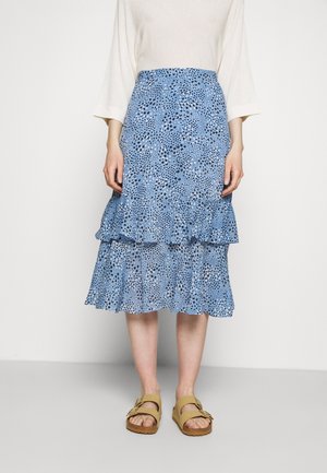 Jupe bleue à volants avec un motif floral, ornée de volants au bas, associée à des sandales beiges. Tissu lisse avec une coupe décontractée.