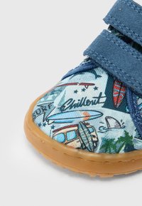 Zbliżenie niebieskiego dziecięcego buta sportowego z ilustracjami w stylu surfingu, w tym deski surfingowe, van, palmy oraz napis „Chillout”.