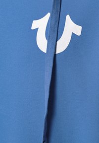 Tissu bleu avec un logo blanc en forme de fer à cheval partiellement recouvert par une fermeture éclair ou une couture verticale bleue au centre.