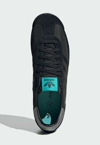 Black athletic shoe with a textured upper, teal accents on the tongue, and silver detailing on the heel. Features traditional lace-up design.