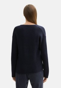 Granatowy sweter z dzianiny o luźnym kroju, z teksturowanym ściągaczem, szerokim dekoltem w serek i opuszczonymi szwami ramion.