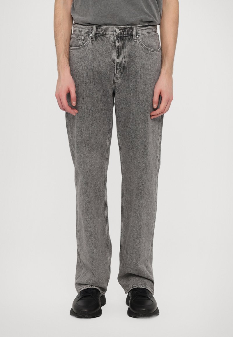 Gray denim jeans with a straight leg design, faded texture, front pockets, and metal hardware, paired with black sneakers.