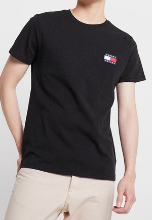 Sort bomulds T-shirt med korte ærmer, rund hals og et lille farverigt logo patch med rød, hvid og blå på brystet.