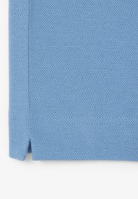 Vaaleansininen teksturoitu kangas, jossa pieni sivuvyöry ja näkyvä ommel reunassa.