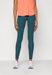 Tealkollekterte tights i elastisk materiale, paret med en korallfarget topp. Skoene er hvite med lilla detaljer. Enkelt design uten synlige mønstre.