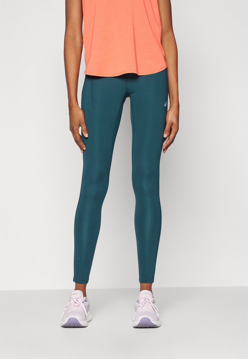 Tealkollekterte tights i elastisk materiale, paret med en korallfarget topp. Skoene er hvite med lilla detaljer. Enkelt design uten synlige mønstre.