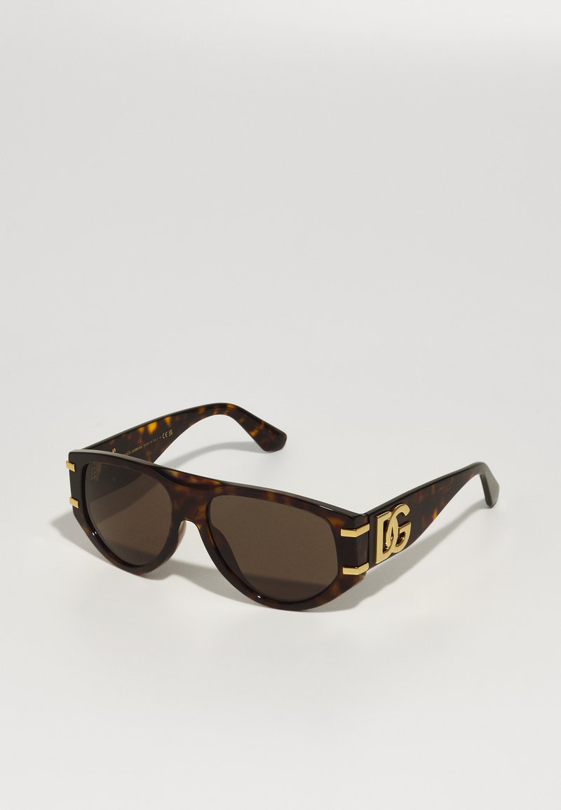 Ochelari de soare din material tortoiseshell cu lentile maronii, design geometric îndrăzneț, accente aurii pe brațe și un logo proeminent pe lateral.