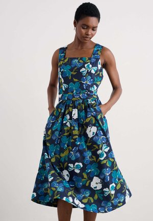 Floral print dress featuring a square neckline, thick straps, and a flared skirt. Predominantly navy blue with green and white accents. Pockets included.
