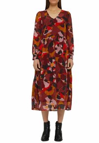 Blommig midiklänning i rika röda och jordnära toner med V-ringning och långa ärmar, som har en flödande silhuett och lager-på-lager kjol. Svarta ankelboots.