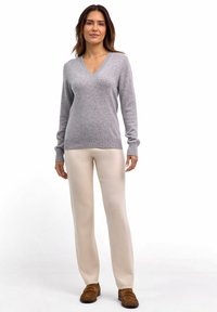 Grauer V-Ausschnitt-Pullover aus weichem Strick, kombiniert mit cremefarbenen, weit geschnittenen Hosen. Das Modell trägt braune Slipper.