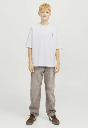 Maglietta bianca in cotone con vestibilità ampia, scollo rotondo e stampa laterale. Abbinata a jeans grigi chiari a vita alta e scarpe da ginnastica marroni.