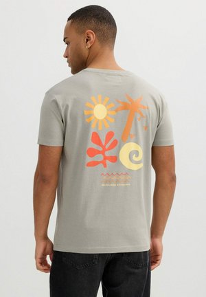 Hombre con camiseta gris con gráficos coloridos de sol, palmera, ola, hoja y espiral y texto "Endless Summer" en la espalda.