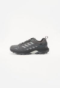 Gray athletic shoe with mesh and suede materials, featuring a thick sole, textured accents, and a lace-up design for support.