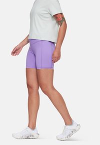 Lila atletiska shorts med en slät textur och en figurnära design. I kombination med en ljusgrön kortärmad t-shirt och vita löparskor.