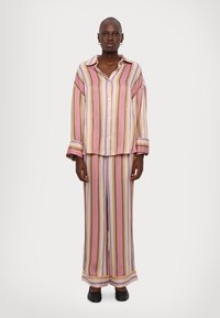 Striped pajama set in pastel colors with pink, yellow, and blue tones. Loose-fitting top and wide-leg pants with cuffed hems. Smooth fabric texture.