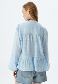 Blusa peplum blu chiaro con una texture a quadretti, maniche lunghe e scollatura rotonda. Abbina a pantaloni corti in denim, con un orlo a più strati.