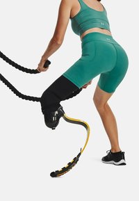 Top atlético ajustado y corto en color azul verdoso; lleva una pierna protésica negra con un pie curvo amarillo; usando cuerdas negras gruesas para hacer ejercicio.