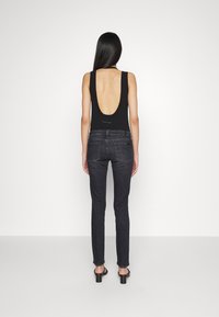 Bodysuit negro con un escote profundo en la espalda, combinado con jeans ajustados gris oscuro. La modelo lleva sandalias de tacón negras. Diseño minimalista, textura suave.