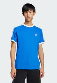 Blue cotton t-shirt with white ribbed collar and sleeves, featuring white three-stripes on shoulders and small Adidas logo on chest.