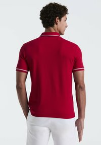 Chemise polo rouge avec une texture unie, dotée d'un col et de accents aux manches blancs. Coupe ajustée, avec des manches courtes et un ourlet droit.