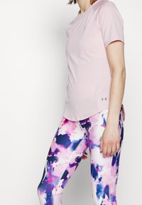Camiseta deportiva de color rosa claro con mangas cortas, combinada con leggins multicolores que presentan un patrón abstracto en púrpura y rosa.