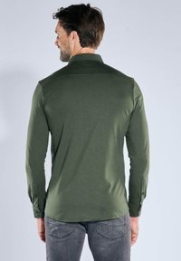 Dunkelgrünes Langarmhemd mit Standardkragen, geknöpften Manschetten und glatter Textur, kombiniert mit grauen Jeans.