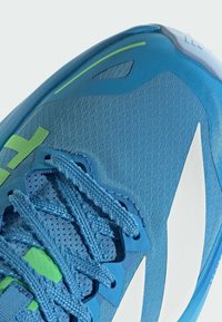 Blauwe sportschoen met een gestructureerd bovenwerk, platte veters, een groen accent en een gedurfd wit logo. Gebogen design met een stabiele zool.