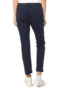 Marinblå tapered byxor med en mjuk textur, som har två bakfickor och en midjeresår med flexibel panel. Bärs med ljusfärgade skor.