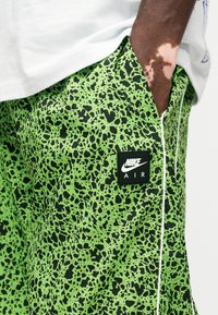 Zöld rövidnadrág, merész fekete pettyes mintával, könnyű anyagból készült, elöl zsebén Nike Air logóval.