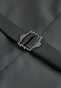 Schwarzer Nylonstoff mit glatter Textur besitzt eine metallische Schnalle in der Mitte. Die Schnalle hat ein elegantes, kantiges Design mit mattem Finish.