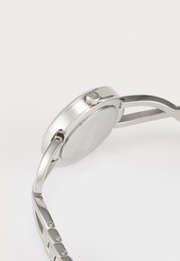 Montre en métal argenté avec un boîtier rond, finition lisse et un seul bouton-poussoir. Présente un bracelet à maillons avec des accents polis.
