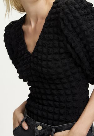 Czarny top o fakturze, z dekoltem w serek, bufkami na rękawach i pofałdowanym wzorem. Połączony z ciemnymi spodniami z denimu, podkreślającymi detale jego designu.