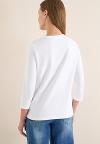 Chemise blanche à manches longues avec un col rond, un tissu en coton doux et une coupe décontractée, associée à un jean en denim bleu clair.