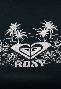 Λευκό τροπικό σχέδιο με φοίνικες, πουλιά, λουλούδια ιβίσκου και τη λέξη "ROXY" κάτω από ένα στυλιζαρισμένο λογότυπο καρδιάς σε μαύρο ύφασμα.