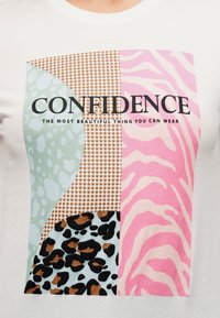 Μπροστινή πλευρά μπλουζάκι με το κείμενο "ΑΥΤΟΠΕΠΟΙΘΗΣΗ" και τη φράση "ΤΟ ΠΙΟ ΟΜΟΡΦΟ ΠΟΥ ΜΠΟΡΕΙΣ ΝΑ ΦΟΡΕΣΕΙΣ" πάνω από ροζ, καφέ, πράσινα και μαύρα μπλοκ με ζωικό μοτίβο.