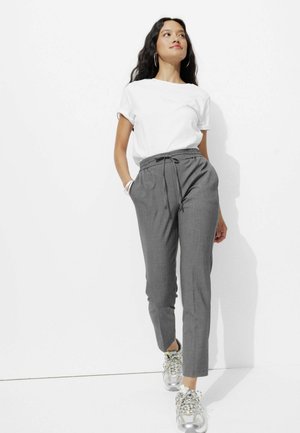 Pantalons gris ajustés avec une taille à cordon, assortis d'un t-shirt blanc uni et de baskets chunky. Texture lisse et coupe slim.