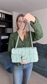 Pikowana torba w kolorze mięty z srebrną klamrą, łańcuszkowym paskiem i teksturowaną powierzchnią, trzymana przed osobą na neutralnym tle.