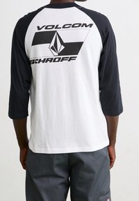 Herrers raglan T-shirt med sorte ærmer og hvid krop. Har et stort sort grafisk print med "VOLCOM" og "SCHROFF" på ryggen.