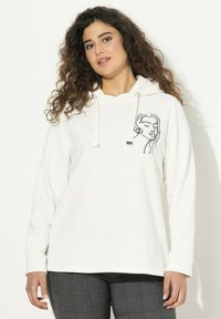 Felpa bianca con cappuccio e coulisse, decorata con un design di volto in line art nero sul lato sinistro del petto. Tessuto morbido e vestibilità ampia, abbinata a pantaloni a quadri.