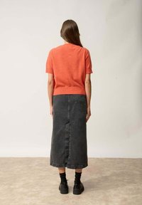 Korallfärgad kortärmad tröja i kombination med en svart denim maxi kjol. Kjolen har en mittsöm och sidofickor, bar med svarta skor.